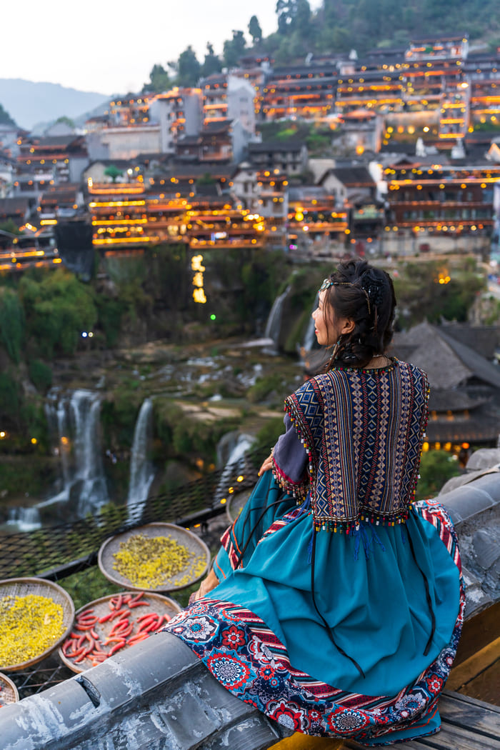 Mujer con vestimenta tradicional China sentada mirando un paisaje de la ciudad